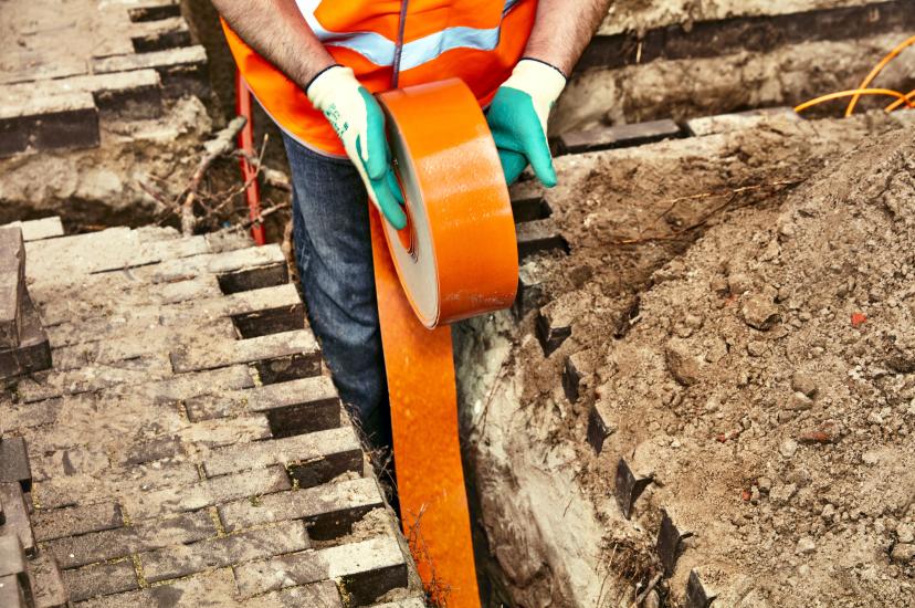 engineer installing orange fibre optic cable in the ground