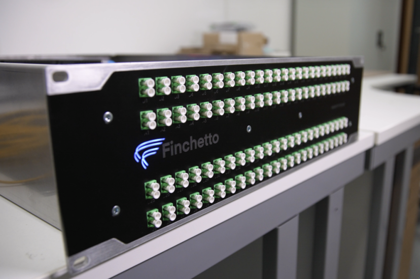 A black rack-mounted network device by Finchetto with rows of green optical fibre connectors