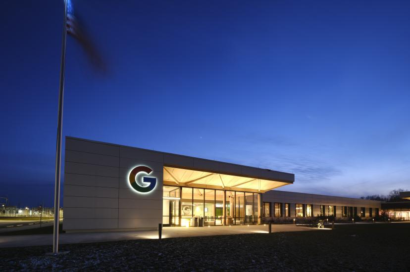 Exterior view of the Google New Albany data centre hub at twilight, featuring the illuminated Google logo on a modern white building facade with an American flag in the foreground