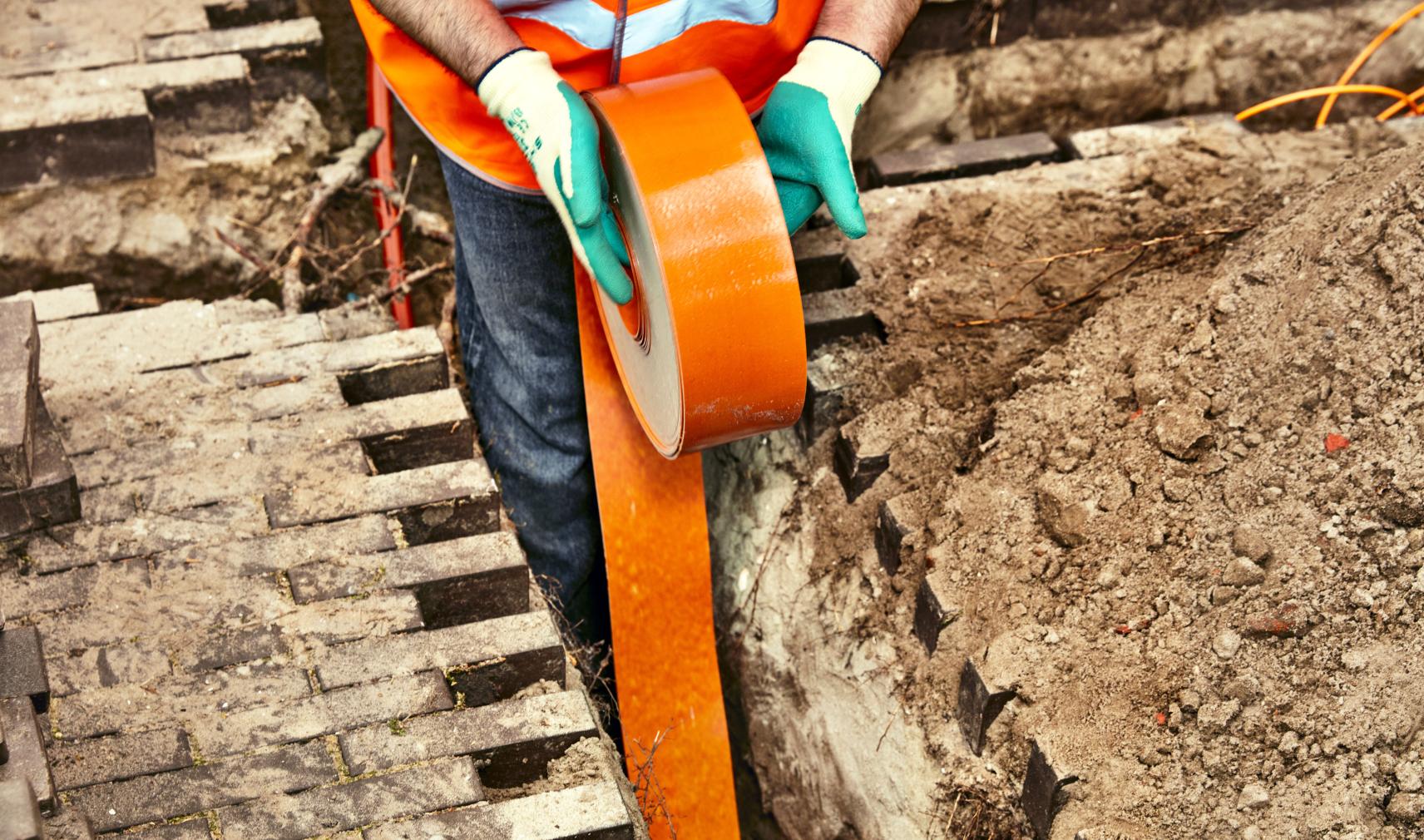engineer installing orange fibre optic cable in the ground