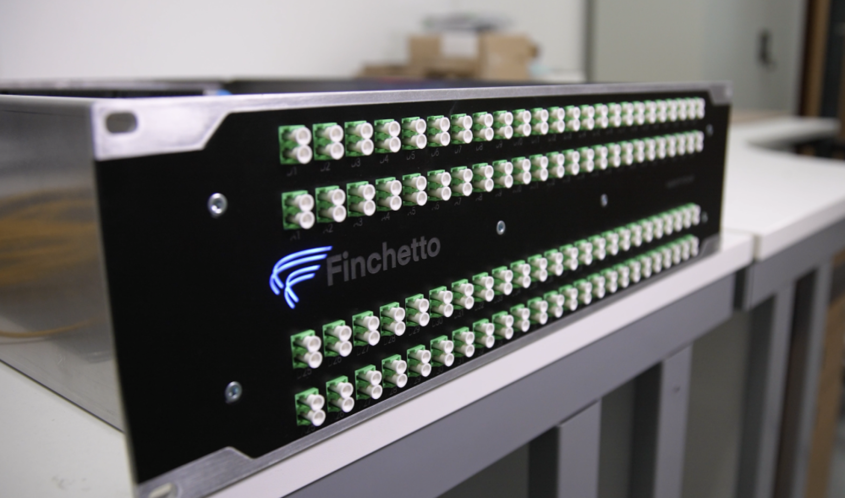 A black rack-mounted network device by Finchetto with rows of green optical fibre connectors