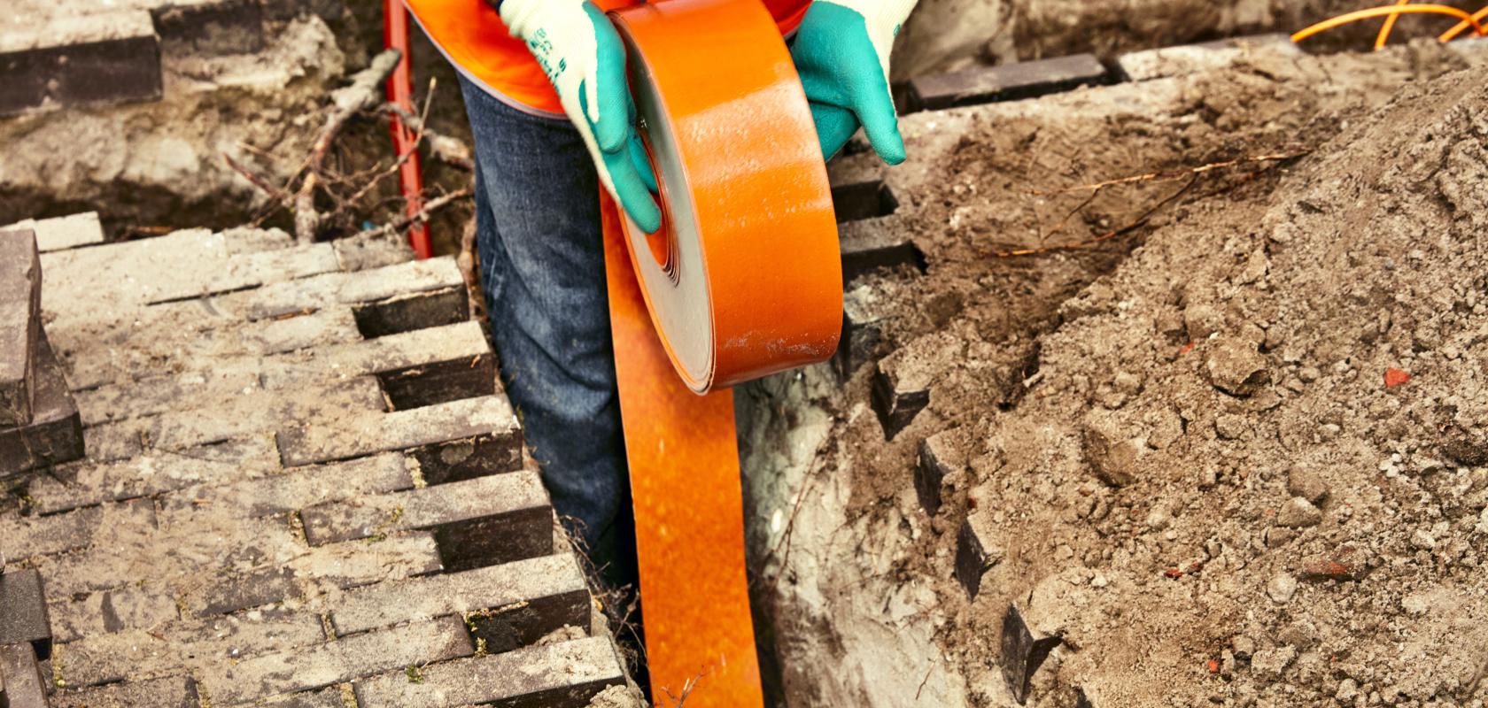 engineer installing orange fibre optic cable in the ground