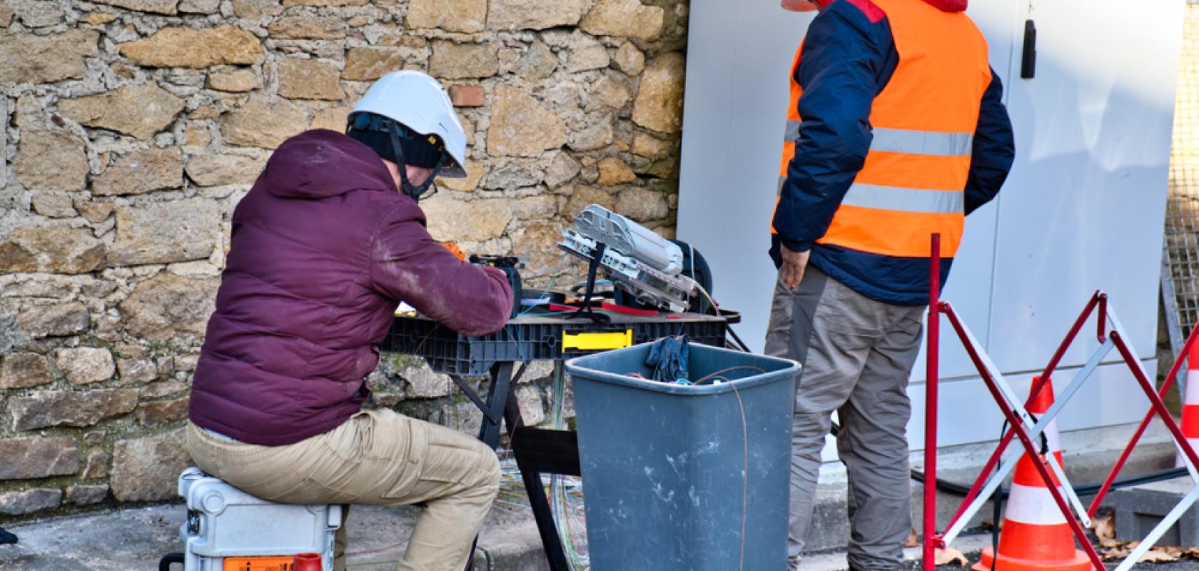 Workers in hard hats and high vis clothing installing fibre optics cables for communications - image is set in France but to represent Germany copper network shutdown