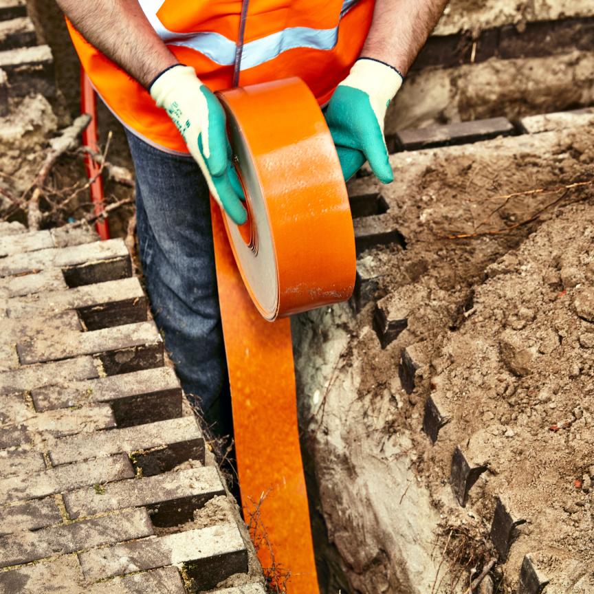 engineer installing orange fibre optic cable in the ground