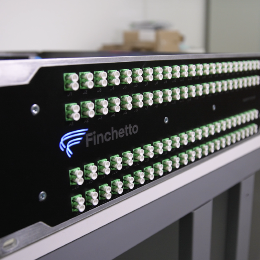 A black rack-mounted network device by Finchetto with rows of green optical fibre connectors